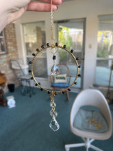 Load image into Gallery viewer, Decorative hanging ornament with crystals and beads held in front of a room interior.
